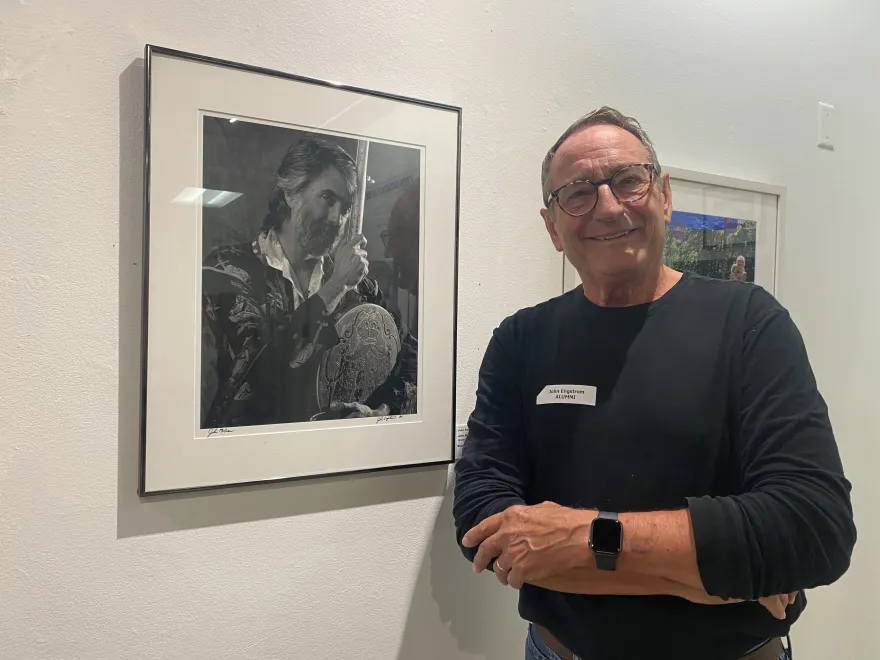 a photo of an NHCC alumni smiling next to a photo he took in the gallery