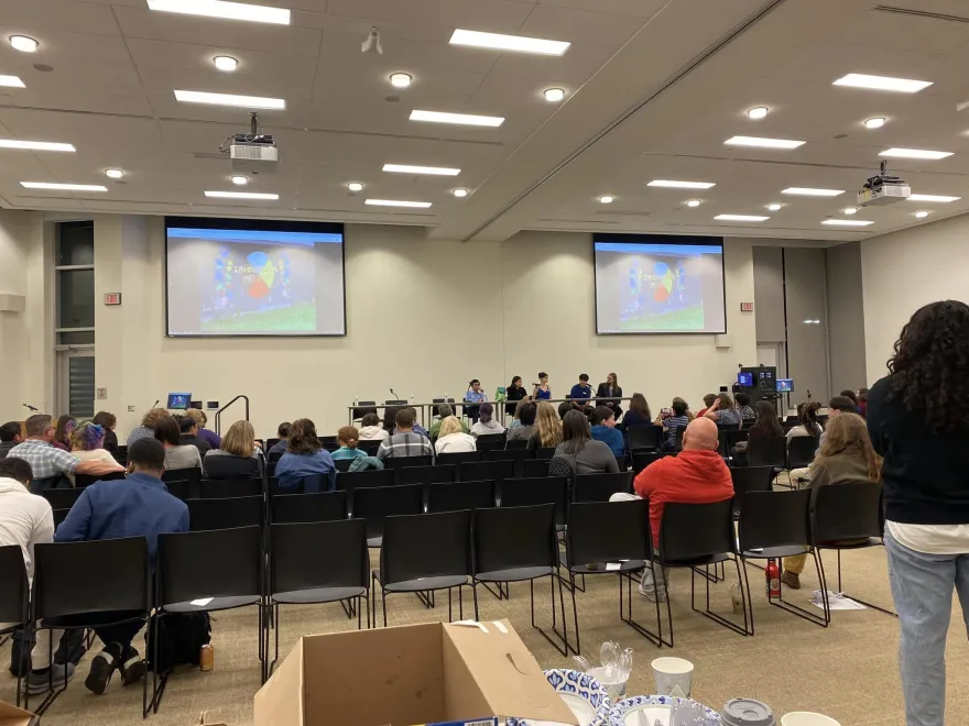 a photo of a group of people in the Grand Hall watching a film on a projector, with a panel of students sitting at the front of the room speaking into a shared microphone. 