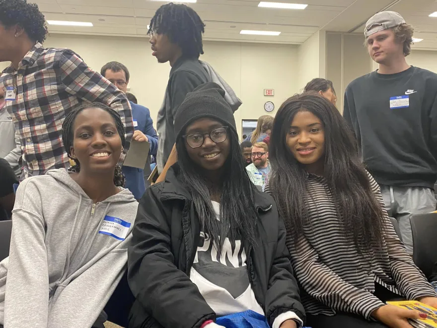 a group of three female students sitting in chairs in the Grand Hall smiling for the camera at an event. 