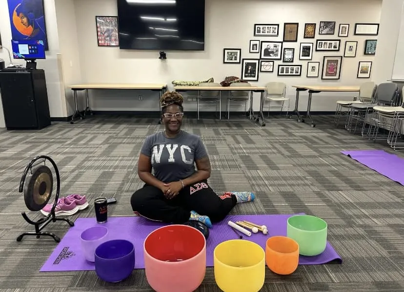 a photo of special guest, Ms. Aja King, in the Campus Center, sitting crosslegged on the ground and smiling. 