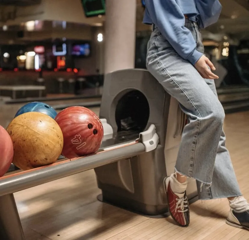 a photo of a person leaning up against the bowling ball retrieval machine at a bowling alley. 