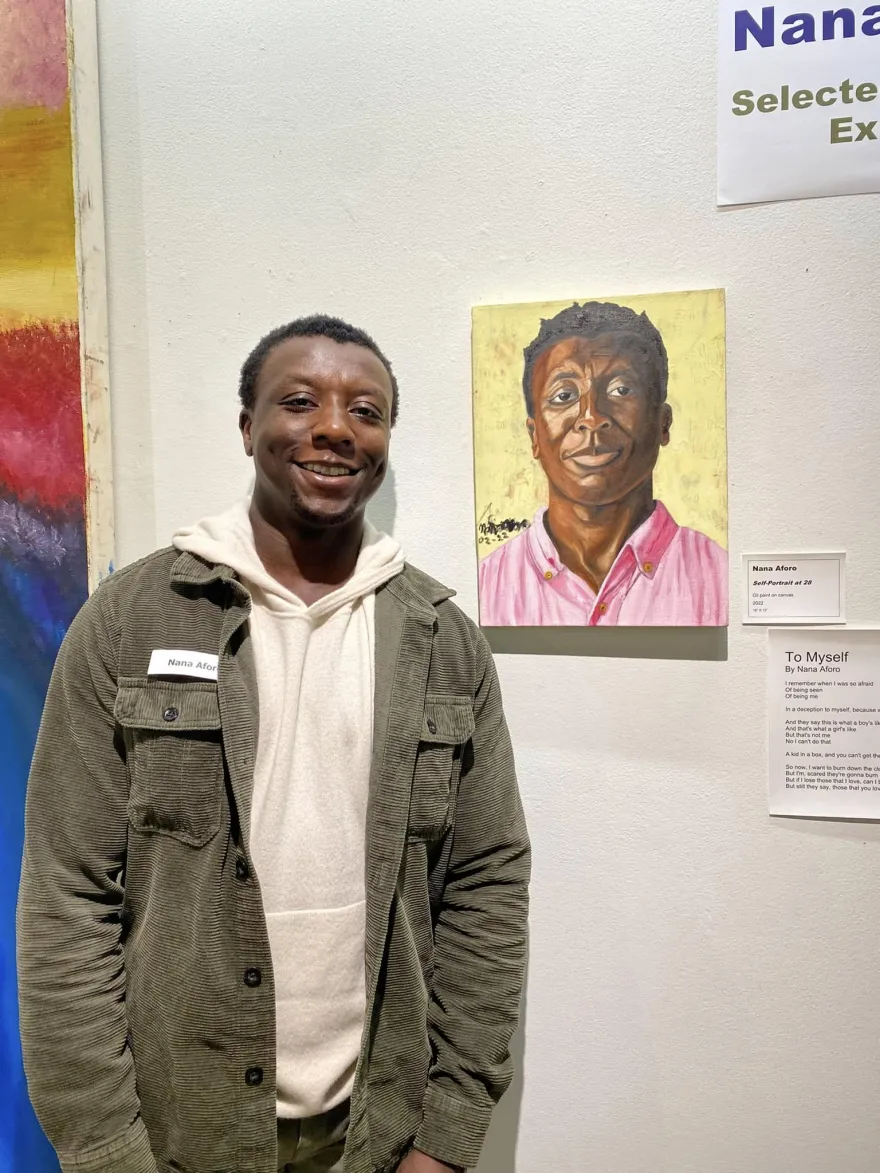 a photo of local artist, Nana Aforo standing next to his painted self portrait in NHCC's Art Gallery.