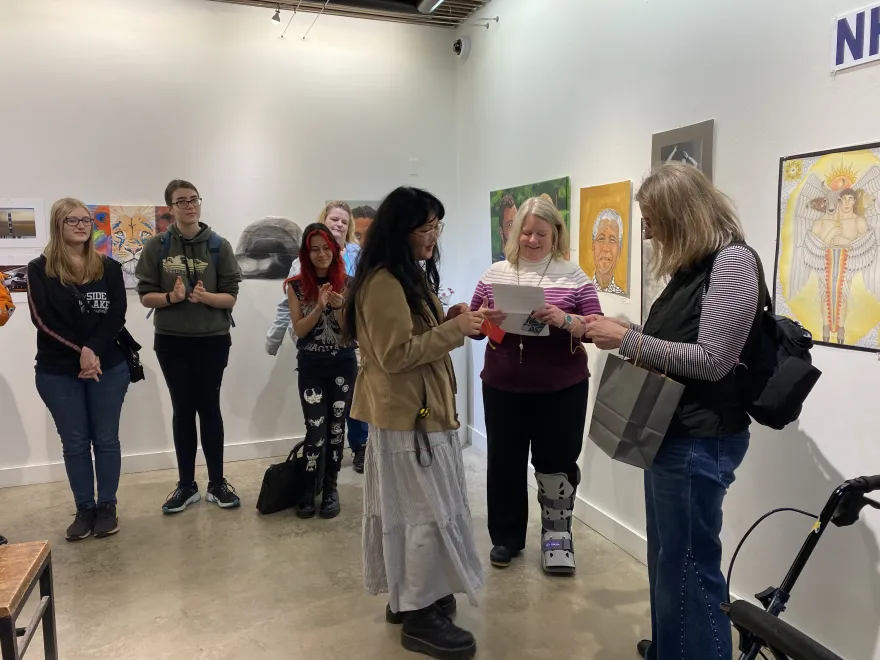 This is a photo of NHCC student, Loveisajoy Pha receiving an award ribbon at the 2025 Student Art Show. 