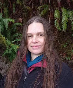 woman smiling outdoors with tress behind her