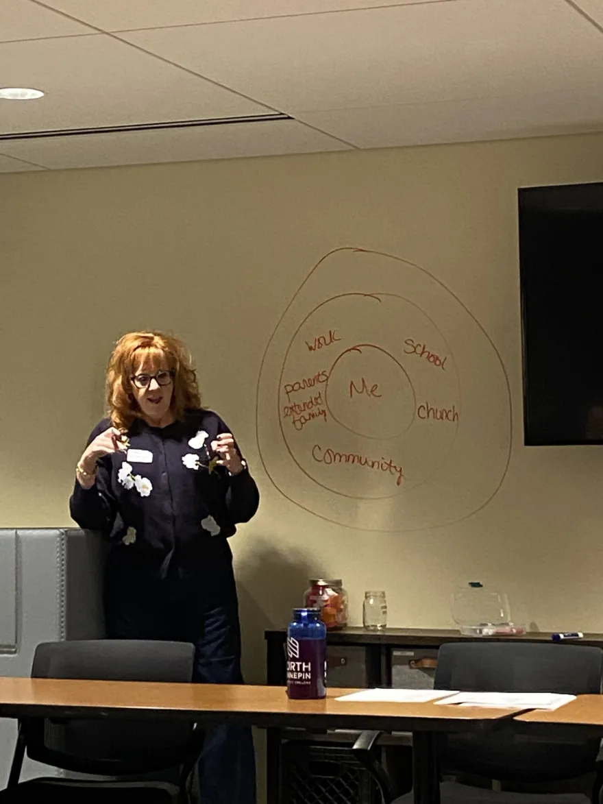 this is a photo of NHCC faculty Amy Harms Hoad presenting off campus in Golden Valley at PRISM next to a whiteboard. 