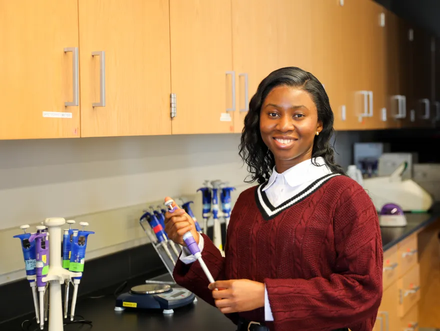 this is a photo of NHCC biology student, Danista Kannah at NHCC in a biology lab, smiling at the camera, while holding a micropipette, scientific tool.  