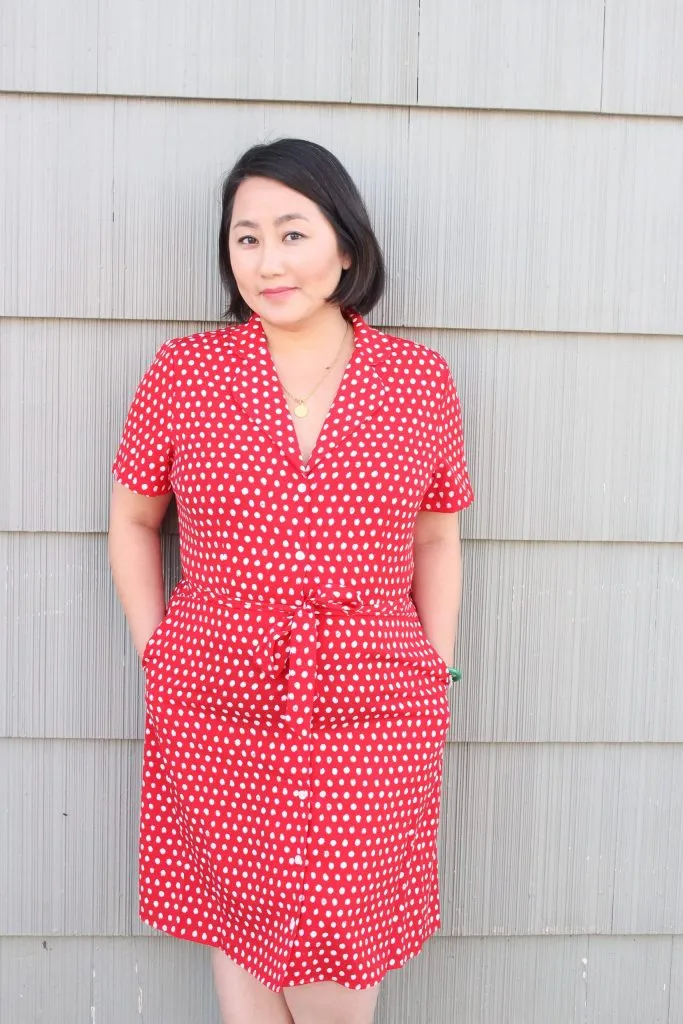 This is a photo of Minnesota author, Kao Kalia Yang, wearing a red dress and leaning against a wall, smiling in her author bio photo.  