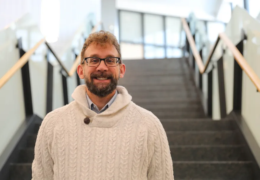 this is a smiling headshot photo of new NHCC Foundation employee, Logan Spindler. This photo was taken in NHCC's CBT building and Logan is standing on the staircase. 