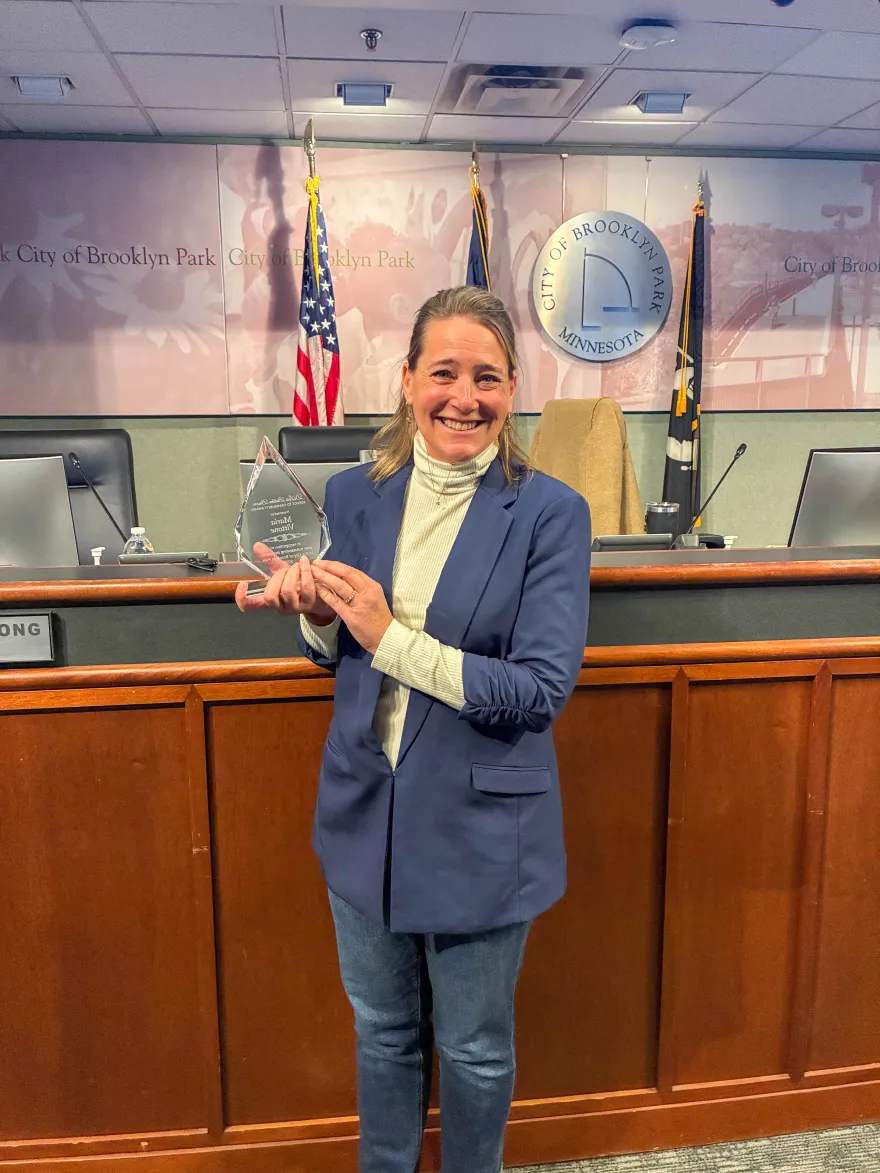 this is a photo of NHCC staff, Maria Vittone, holding an award as she was honored during a City Council meeting at the Brooklyn Park City Hall. 
