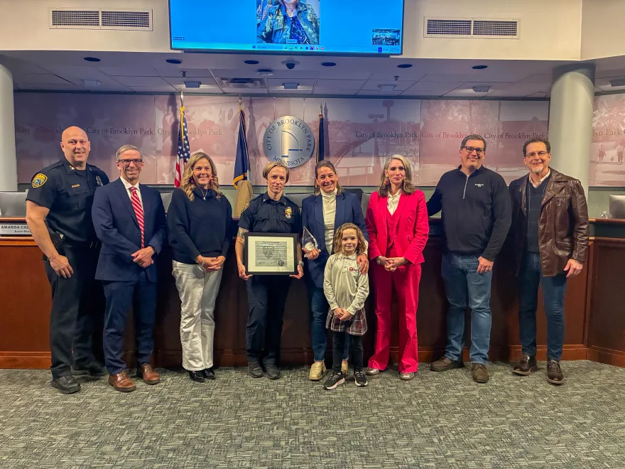 this is a group photo of NHCC staff, Maria Vittone, gathered around by many various people from the City of Brooklyn Park, pictured at City Hall. 