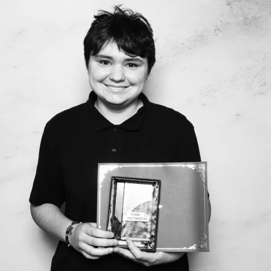 this is a black and white photobooth photo of NHCC student, Robin smiling and holding up his Student Life Award certificate.