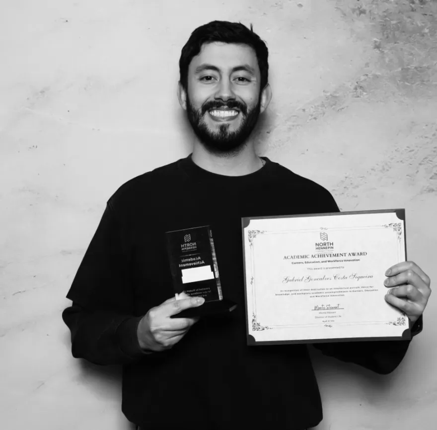 this is a black and white photobooth photo of NHCC student, Gabriel smiling and holding up his Student Life Award certificate.