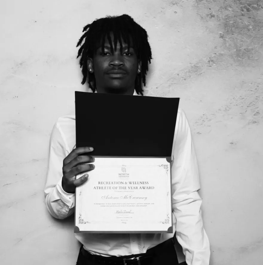 this is a black and white photobooth photo of NHCC student, Antonio smiling and holding up his Student Life Award certificate.