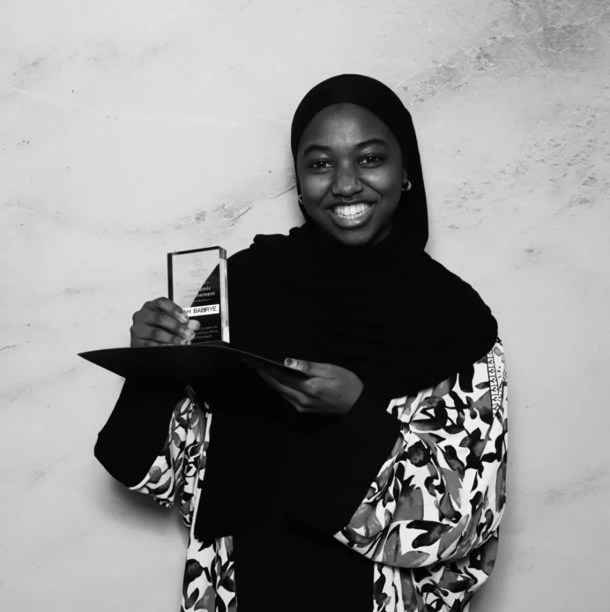this is a black and white photobooth photo of NHCC student, Nurah smiling and holding up her Student Life Award certificate.