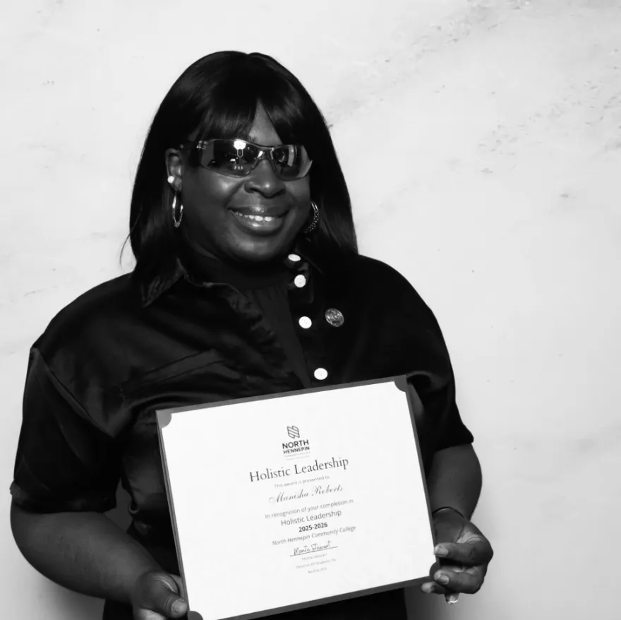 this is a black and white photobooth photo of NHCC student, Manisha smiling and holding up her Student Life Award certificate.