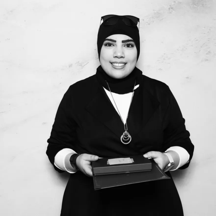 this is a black and white photobooth photo of NHCC student, Muna smiling and holding up her Student Life Award certificate.