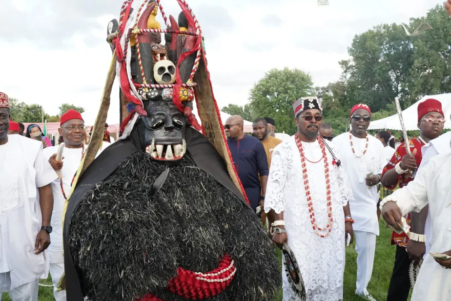A traditional masquerade performer wearing an ornate black costume and ceremonial headdress participates in a cultural procession during IgboFest.