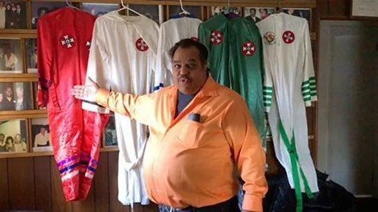 Man pointing to robes that are hanging behind him. 
