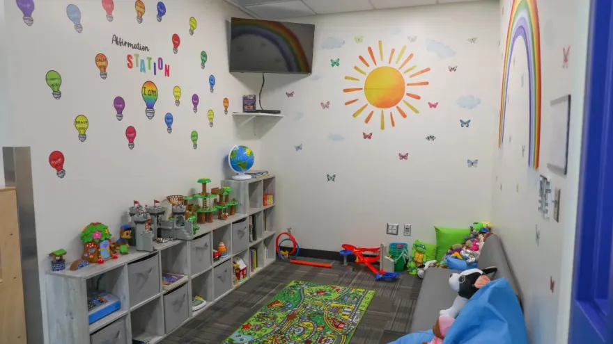 this is a photo of NHCC's Student Parent Resource Room. It shows a couch, kids toys, a tv in the corner and bright, colorful images and uplifting phrases for kids on the wall. 