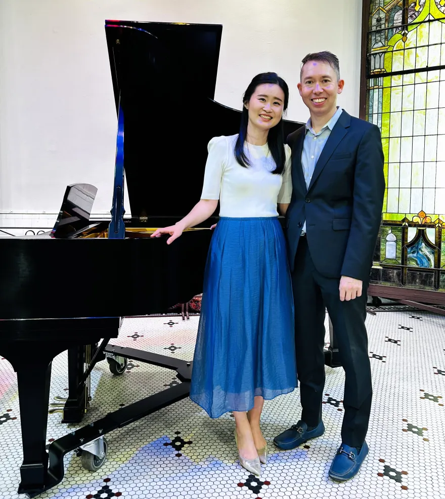this is a smiling photo of NHCC music faculty, Grace Choi and Kevin Hobbs standing next to a piano. 