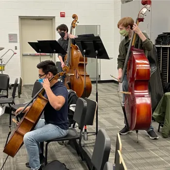 3 students, a cellist and 2 bassists, rehearsing in orchestra room 