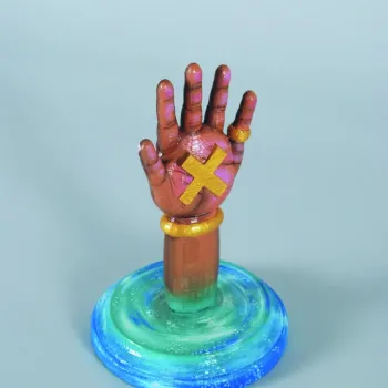 sculpture of a hand with a yellow x on palm, coming out of a blue disk