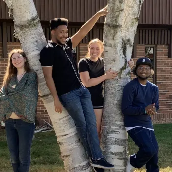 Four students from the Creative Writing Club pose outside of the HWC building next to a tree. 