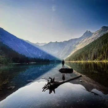 photo of mountains reflecting on a lake with a person standing on a boat