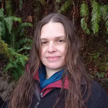 woman smiling outdoors with tress behind her