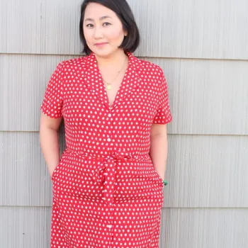 This is a photo of Minnesota author, Kao Kalia Yang, wearing a red dress and leaning against a wall, smiling in her author bio photo.  